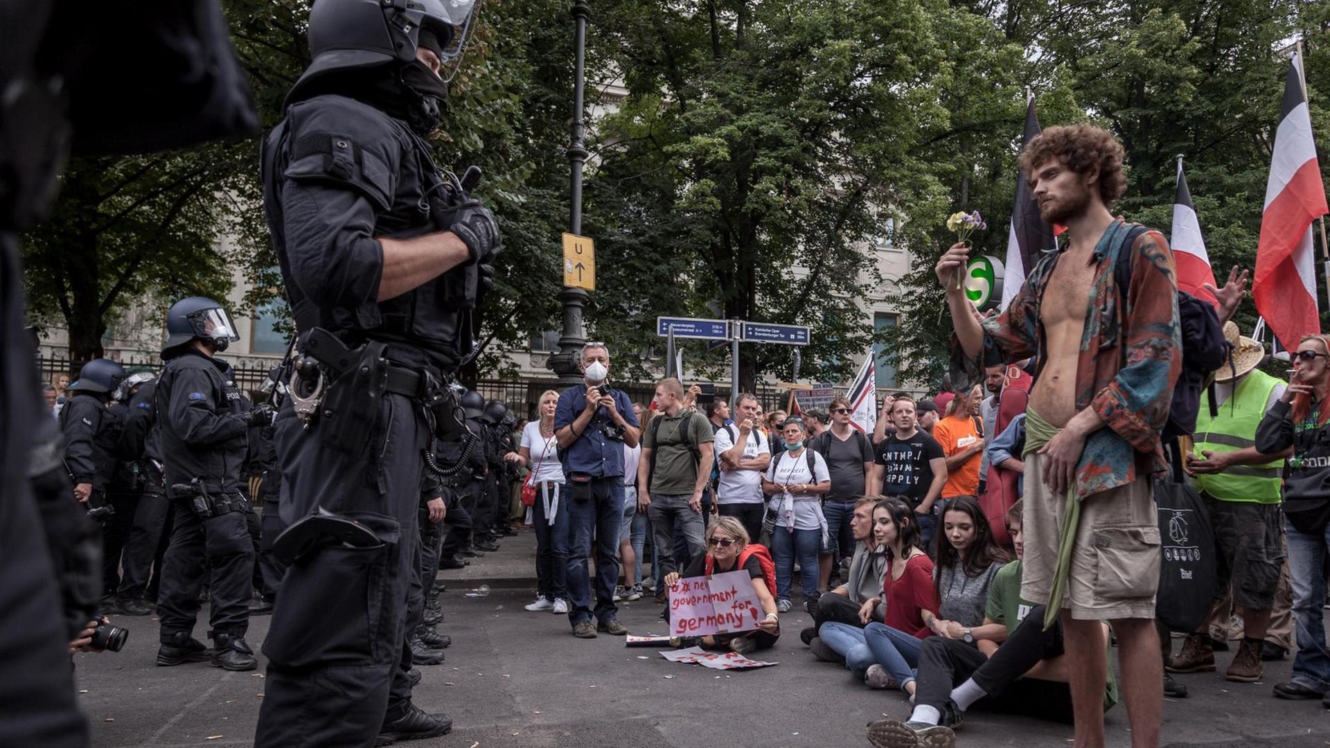 Eine Straßenszene während der Demonstration gegen die Corona-Maßnahmen am 29. August in Berlin. Darauf zu sehen ist ein Polizist, der diversen Demonstranten gegenüber steht. Einer davon hält in hippiesker Kleidung eine Blume in der Hand. Hinter ihm sind schwarz-weiß-rote Reichskriegsflagge aus Zeiten des Deutschen Kaiserreich zu sehen. Eine Straßenszene während der Demonstration gegen die Corona-Maßnahmen am 29. August in Berlin. Darauf zu sehen ist ein Polizist, der diversen Demonstranten gegenüber steht. Einer davon hält in hippiesker Kleidung eine Blume in der Hand. Hinter ihm sind schwarz-weiß-rote Reichskriegsflagge aus Zeiten des Deutschen Kaiserreich zu sehen.