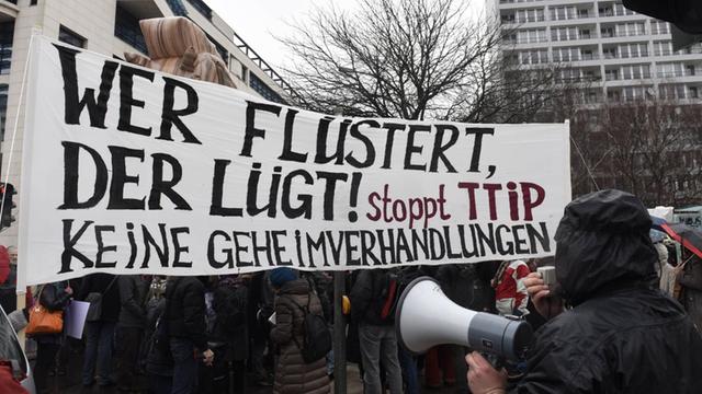 Demonstranten halten ein Schild mit der Aufschrift "Wer flüstert der lügt! Stoppt TTIP! Keine Geheimverhandlungen" hoch.