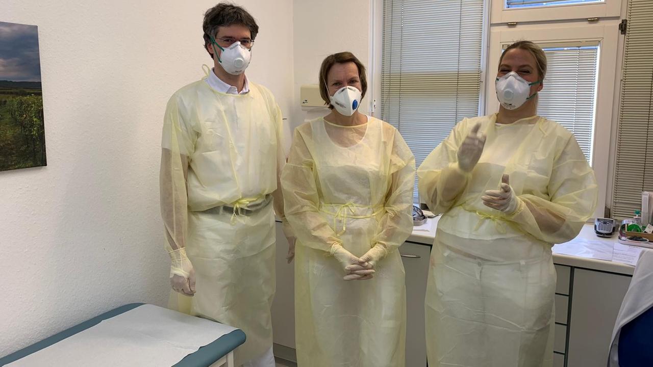 Drei Ärzte in heller Schutzkleidung stehen in einem Behandlungszimmer. Es die die Praxis Martin Heinert in Bahlingen.