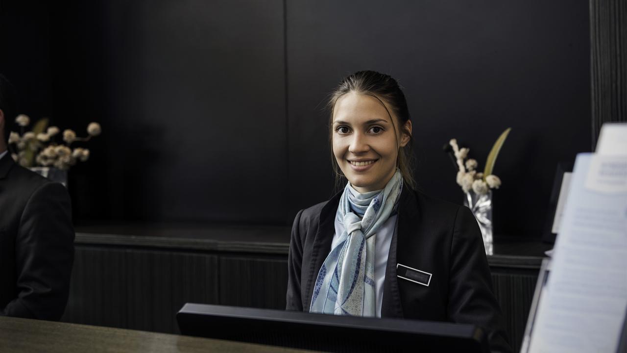 Eine junge Frau sitzt lächelnd hinter einer dem Tresen einer Hotelrezeption. Eine junge Frau sitzt lächelnd hinter einer dem Tresen einer Hotelrezeption.