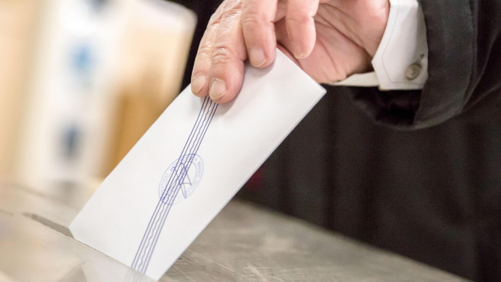 Ein Hand steckt einen Wahlschein in eine Wahlurne.
