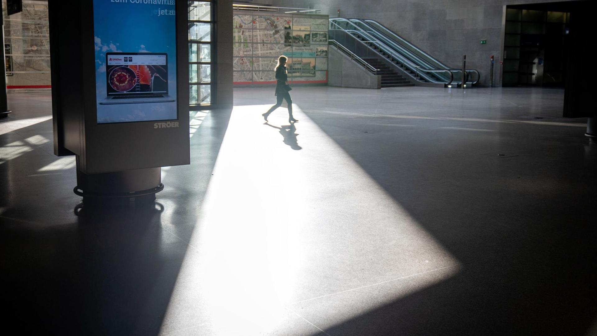 Die Passantin läuft im Gegenlicht einfallender Sonnenstrahlen durch eine menschenleere U-Ebene.