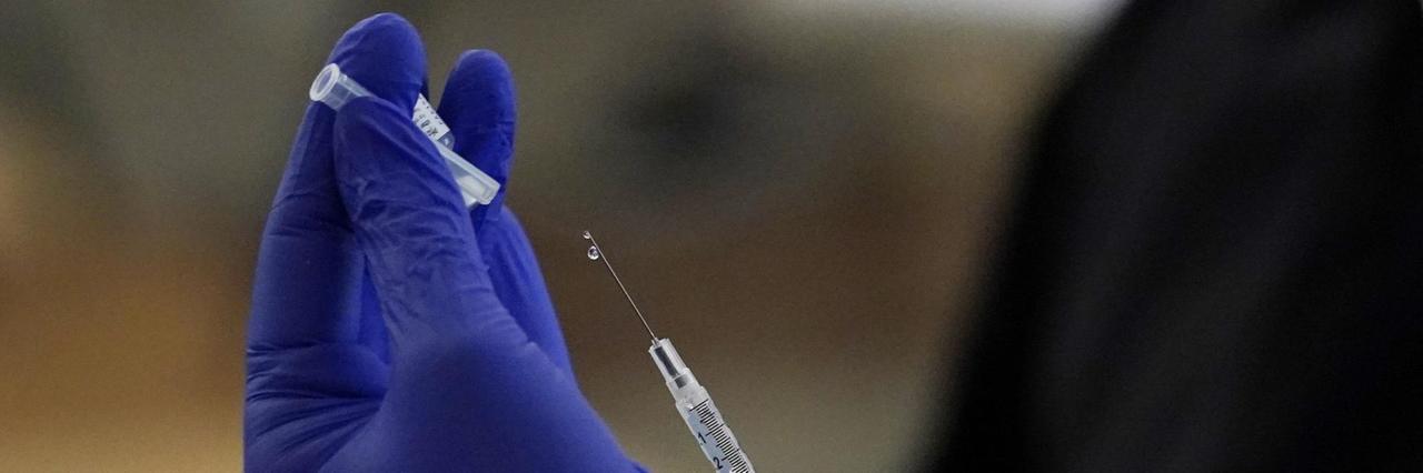 Zwei Hände mit blauen Schutzhandschuhen ziehen eine Spritze zur Impfung auf Zwei Hände mit blauen Schutzhandschuhen ziehen eine Spritze zur Impfung auf