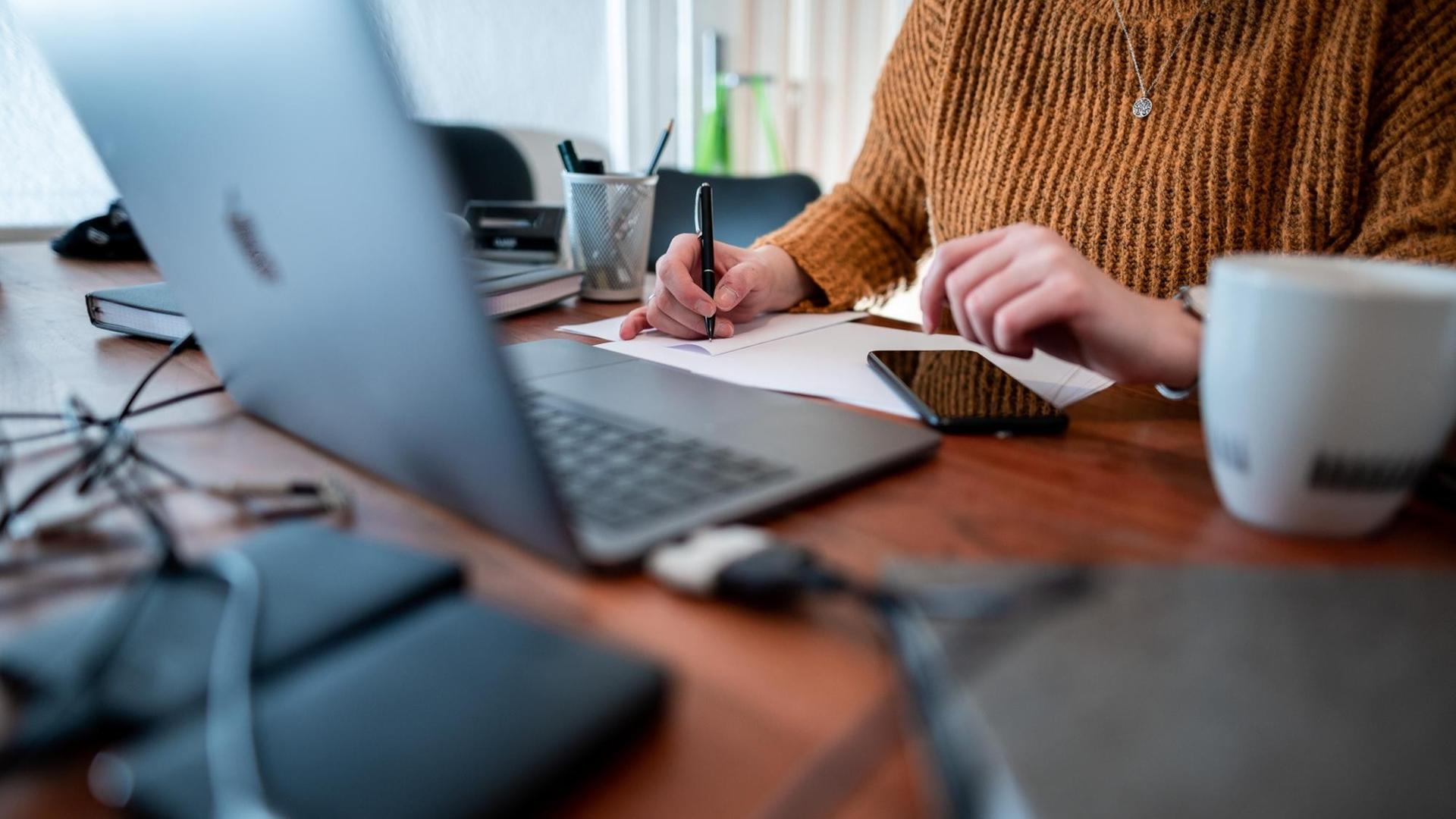 Eine Frau sitzt mit einem Laptop an einem Tisch im Homeoffice. Eine Frau sitzt mit einem Laptop an einem Tisch im Homeoffice.
