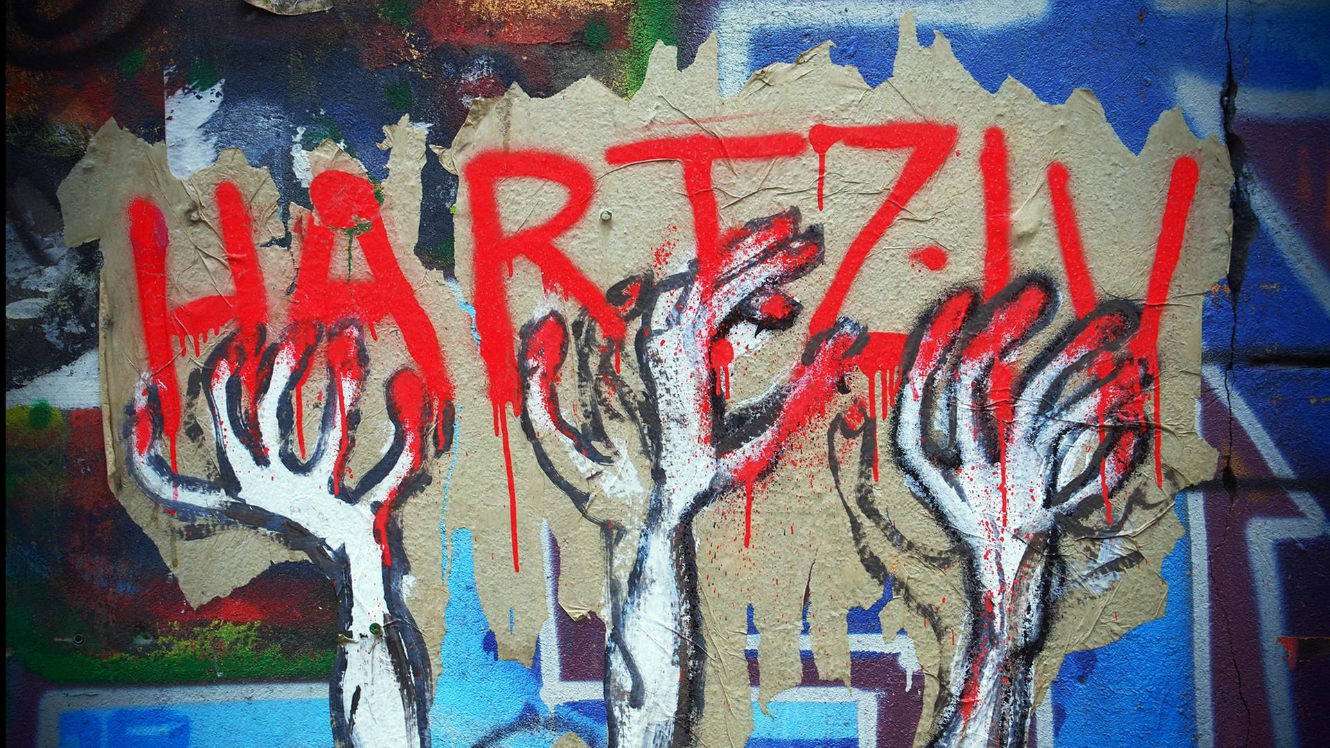 Hartz IV als Graffiti in roter Schrift, nach der dünne, zittrige Hände greifen