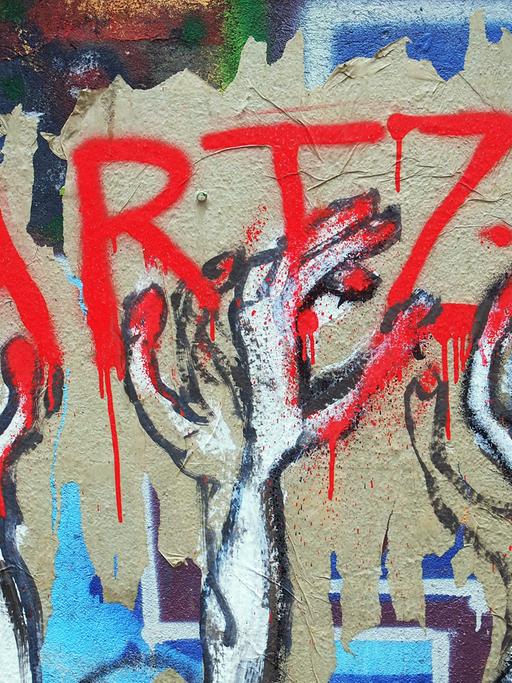 Hartz IV als Graffiti in roter Schrift, nach der dünne, zittrige Hände greifen