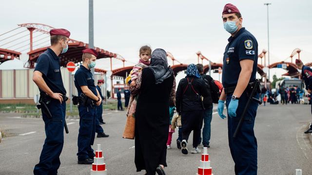 Mehrere Frauen überqueren die Grenze, zu beiden Seiten Grenzschützer. Mehrere Frauen überqueren die Grenze, zu beiden Seiten Grenzschützer.