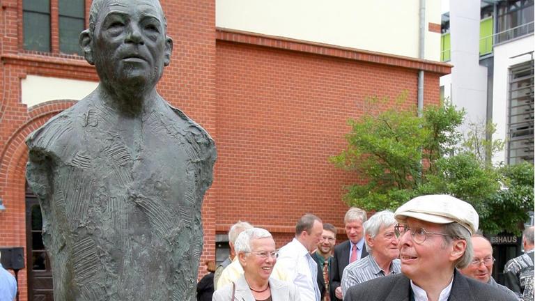 Der Bildhauer Wieland Förster (vorn r.) steht am Freitag (20.07.2007) auf dem Domplatz in Güstrow neben dem von ihm geschaffenen Denkmal für den Schriftsteller Uwe Johnson (1934-1984), das kurz zuvor am 73. Geburtstag von Johnson enthüllt wurde. Die 2,10 Meter hohe Bronzestele steht vor der John-Brinckman-Schule, die Johnson von 1948 bis zum Abitur 1952 besuchte. Die Stele wurde im vergangenen Jahr von dem bei Oranienburg (Brandenburg) lebenden Bildhauer Förster geschaffen. Johnson stammte aus Pommern und zählte mit seinen Werken, die sich meist mit der Ost-West-Problematik beschäftigten, zu den großen Autoren des 20. Jahrhunderts. (zu Meldung lmv 4248 vom 20.07.2007) Foto: Bernd Wüstneck dpa/lmv +++(c) dpa - Report+++ | Verwendung weltweit Der Bildhauer Wieland Förster (vorn r.) steht am Freitag (20.07.2007) auf dem Domplatz in Güstrow neben dem von ihm geschaffenen Denkmal für den Schriftsteller Uwe Johnson (1934-1984), das kurz zuvor am 73. Geburtstag von Johnson enthüllt wurde. Die 2,10 Meter hohe Bronzestele steht vor der John-Brinckman-Schule, die Johnson von 1948 bis zum Abitur 1952 besuchte. Die Stele wurde im vergangenen Jahr von dem bei Oranienburg (Brandenburg) lebenden Bildhauer Förster geschaffen. Johnson stammte aus Pommern und zählte mit seinen Werken, die sich meist mit der Ost-West-Problematik beschäftigten, zu den großen Autoren des 20. Jahrhunderts. (zu Meldung lmv 4248 vom 20.07.2007) Foto: Bernd Wüstneck dpa/lmv +++(c) dpa - Report+++ | Verwendung weltweit