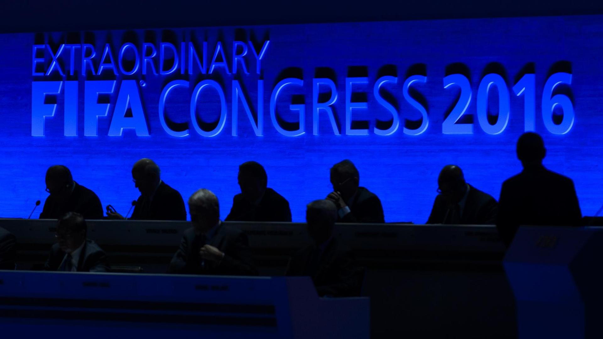 Schwarze Silhouetten vor einer blauen Wand, auf der "Extraordinary FIFA Congress 2016" steht. Schwarze Silhouetten vor einer blauen Wand, auf der "Extraordinary FIFA Congress 2016" steht.