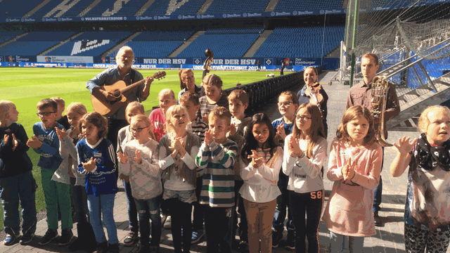 Die Symphoniker Hamburg kommen mit einigen Musikern regelmäßig ins Volksparkstadion, um dort mit Kindern aus bildungsfernen Familien eine Vereinshymne für den HSV zu komponieren.