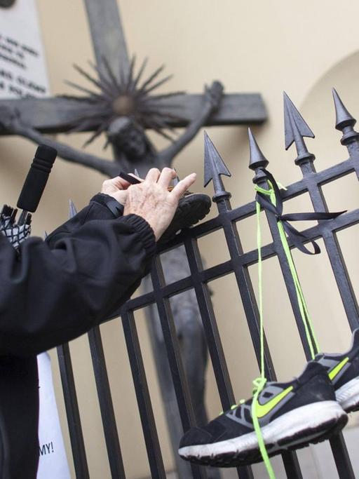 Ein Frau bindet Kinderschuhe an den Zaun einer Kirche