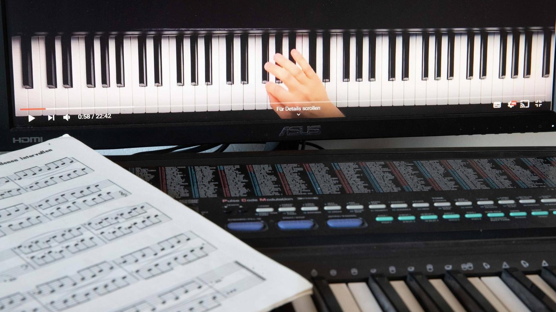 Musikschulunterricht via Skype: Ein Notenblatt liegt auf einem Keyboard, dahinter ist ein Bildschirm aufgebaut, auf dem eine Hand auf einer Klaviertastatur zu sehen ist. Musikschulunterricht via Skype: Ein Notenblatt liegt auf einem Keyboard, dahinter ist ein Bildschirm aufgebaut, auf dem eine Hand auf einer Klaviertastatur zu sehen ist.