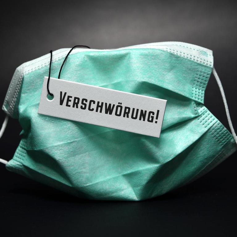 Eine Fotomontage zeigt eine Schutzmaske mit Etikett und der Aufschrift "Verschwörung".