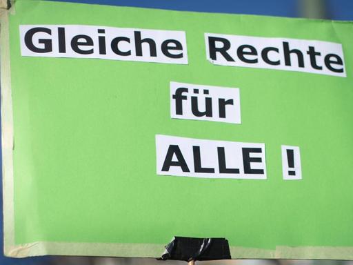 Hellgrünes Schild einer Demonstrantin mit den aus einer Zeitung ausgeschnittenen und aufgeklebten Worten: "Gleiche Rechte für ALLE !"
