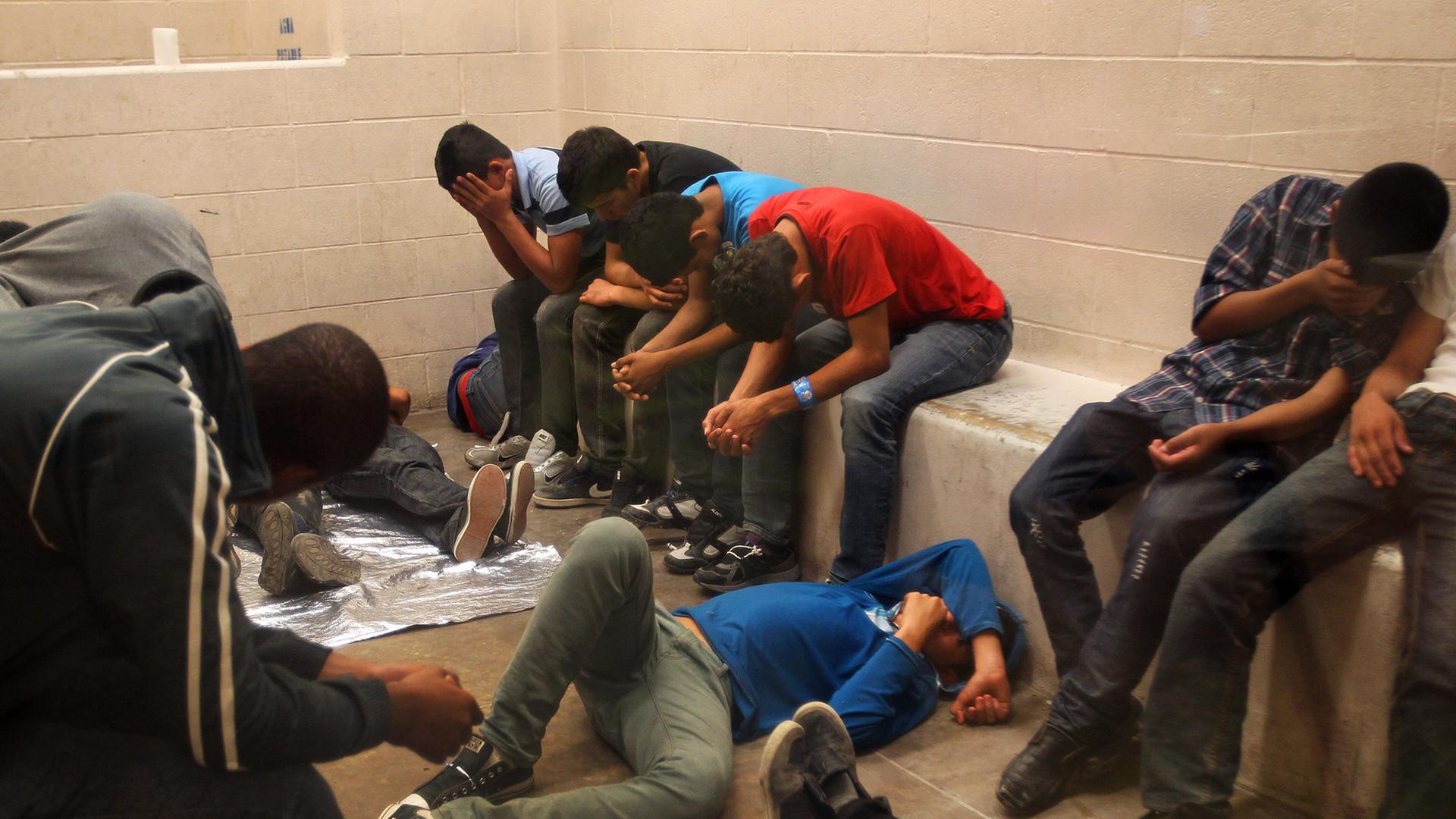 Eine überfüllte Arrestzelle mit einem Dutzend Jugendlicher, die auf Bänken sitzen und auf dem Boden liegen und ihre Gesichter vor der Kamera verbergen