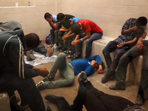 Eine überfüllte Arrestzelle mit einem Dutzend Jugendlicher, die auf Bänken sitzen und auf dem Boden liegen und ihre Gesichter vor der Kamera verbergen