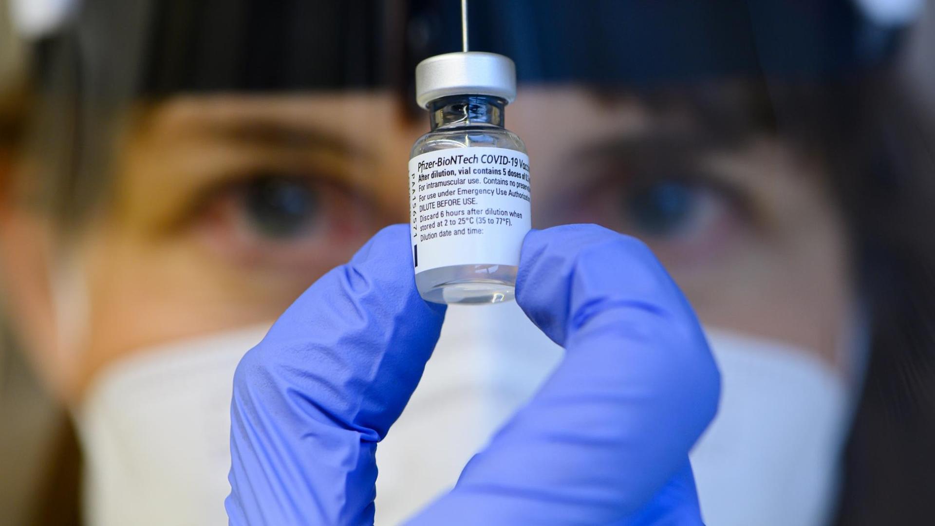 Eine medizinische Fachkraft hält eine Impfdosis zwischen zwei Fingern in die Kamera