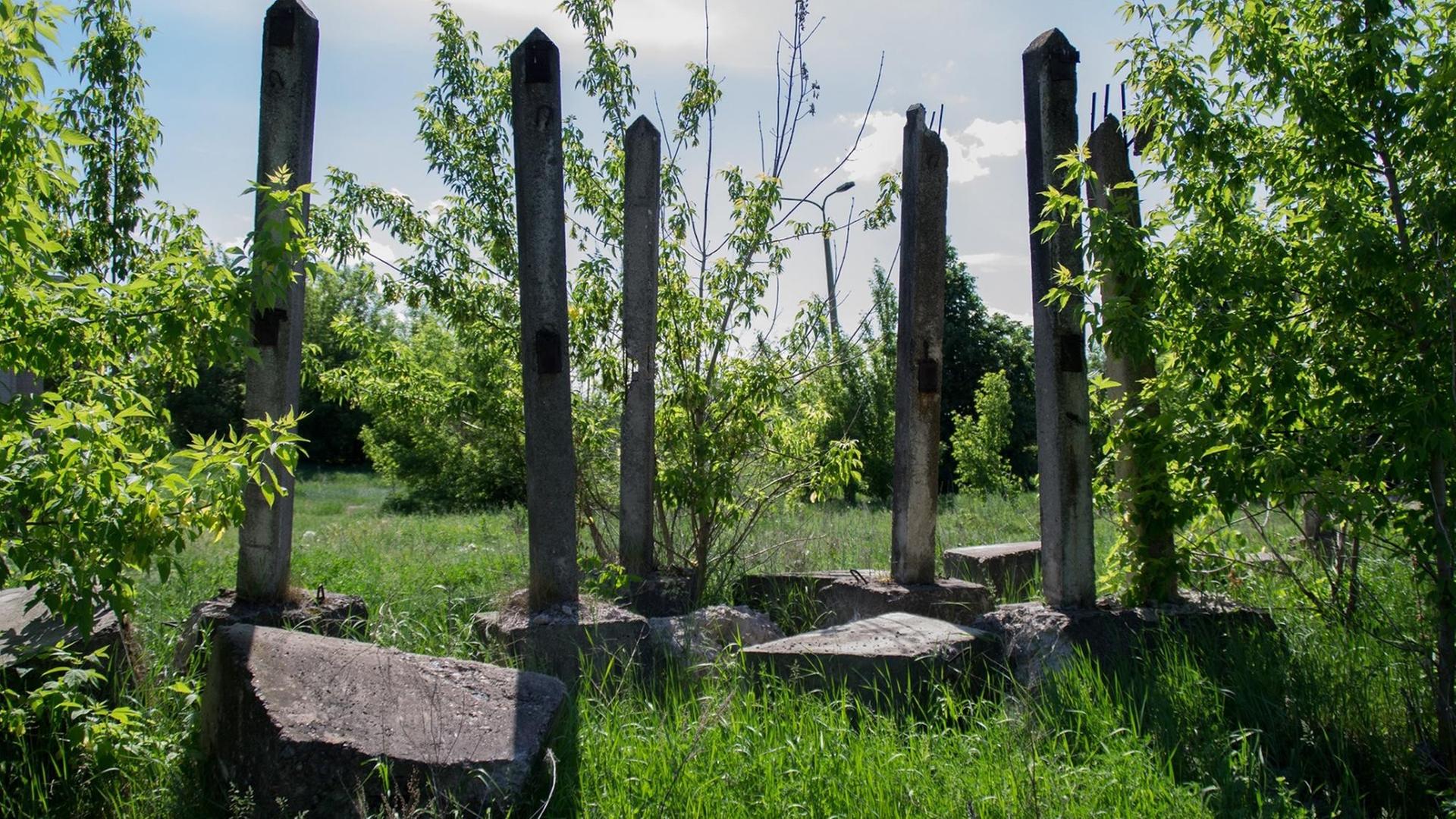 Die Ruinen von Beton auf einer Wiese. Pflanzen überwuchern die abgebrochenen Säulen und Steine. Die Ruinen von Beton auf einer Wiese. Pflanzen überwuchern die abgebrochenen Säulen und Steine.