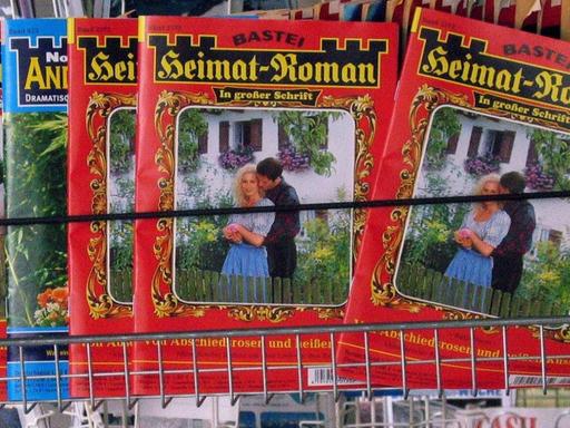 Diverse Printprodukte in der Auslage eines Kiosks, wo insbesondere die Reihe "Heimat-Roman" das Angebot bestimmt, darunter sind weitere Magazine zu sehen.
