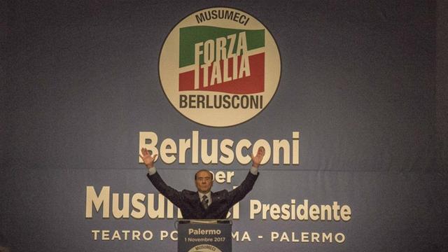 Wahlkampf in Sizilien: Silvio Berlusconi steht in Jubelpose vor seinen Anhängern. Hinter ihm stehen die Namen Berlusconi und Musumeci, der als Kandidat des Rechtsbündnisses bei der Regionalwahl auf Sizilien gewann