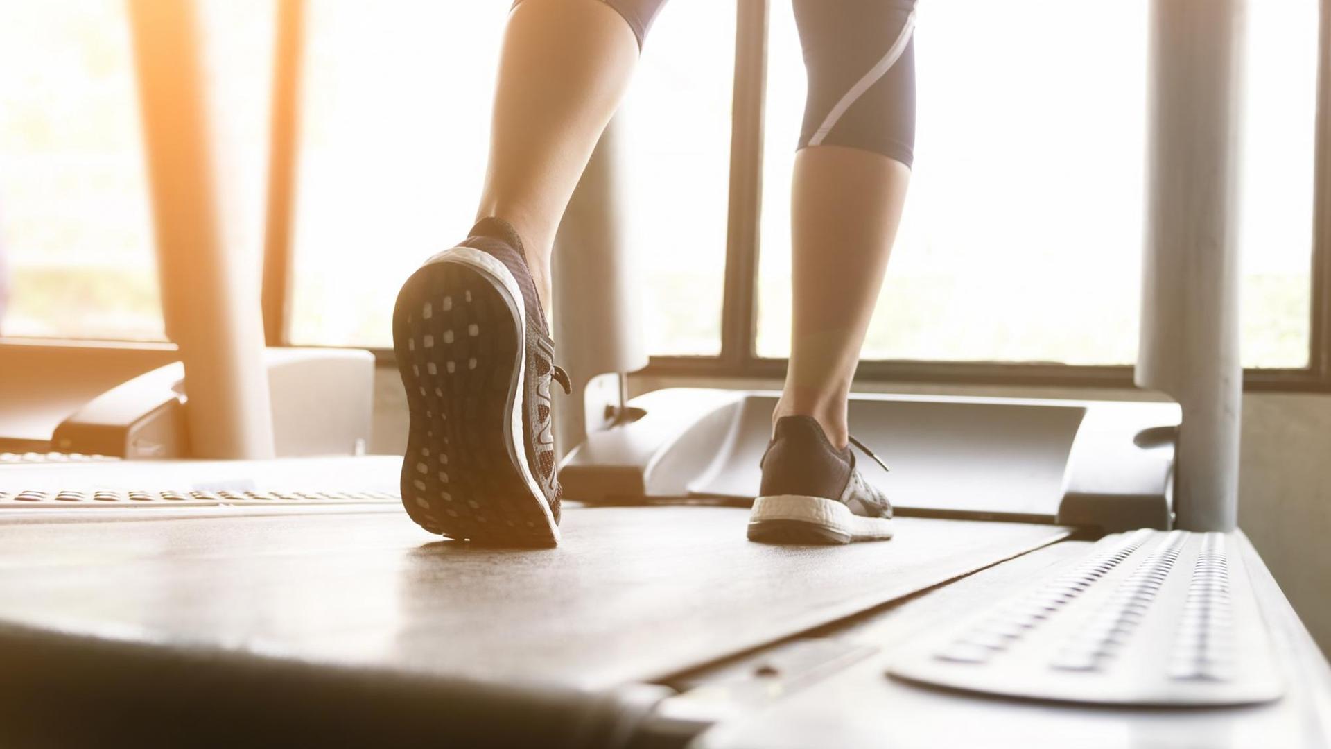 Die Beine einer Frau, die in Sneakers auf einem Laufband läuft. Die Beine einer Frau, die in Sneakers auf einem Laufband läuft.
