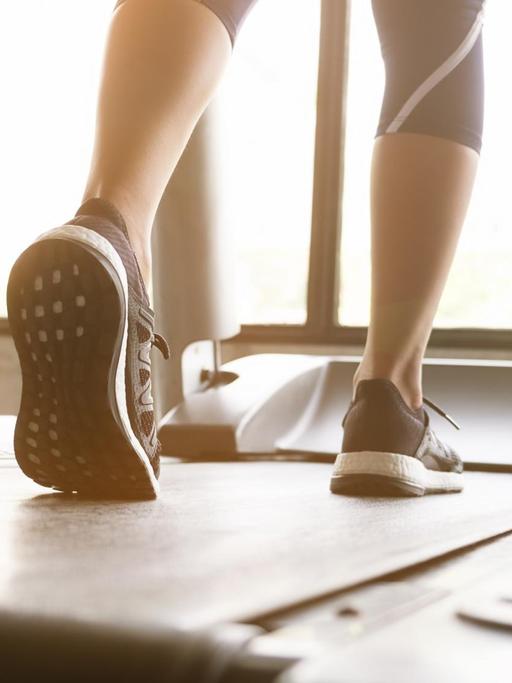 Die Beine einer Frau, die in Sneakers auf einem Laufband läuft.