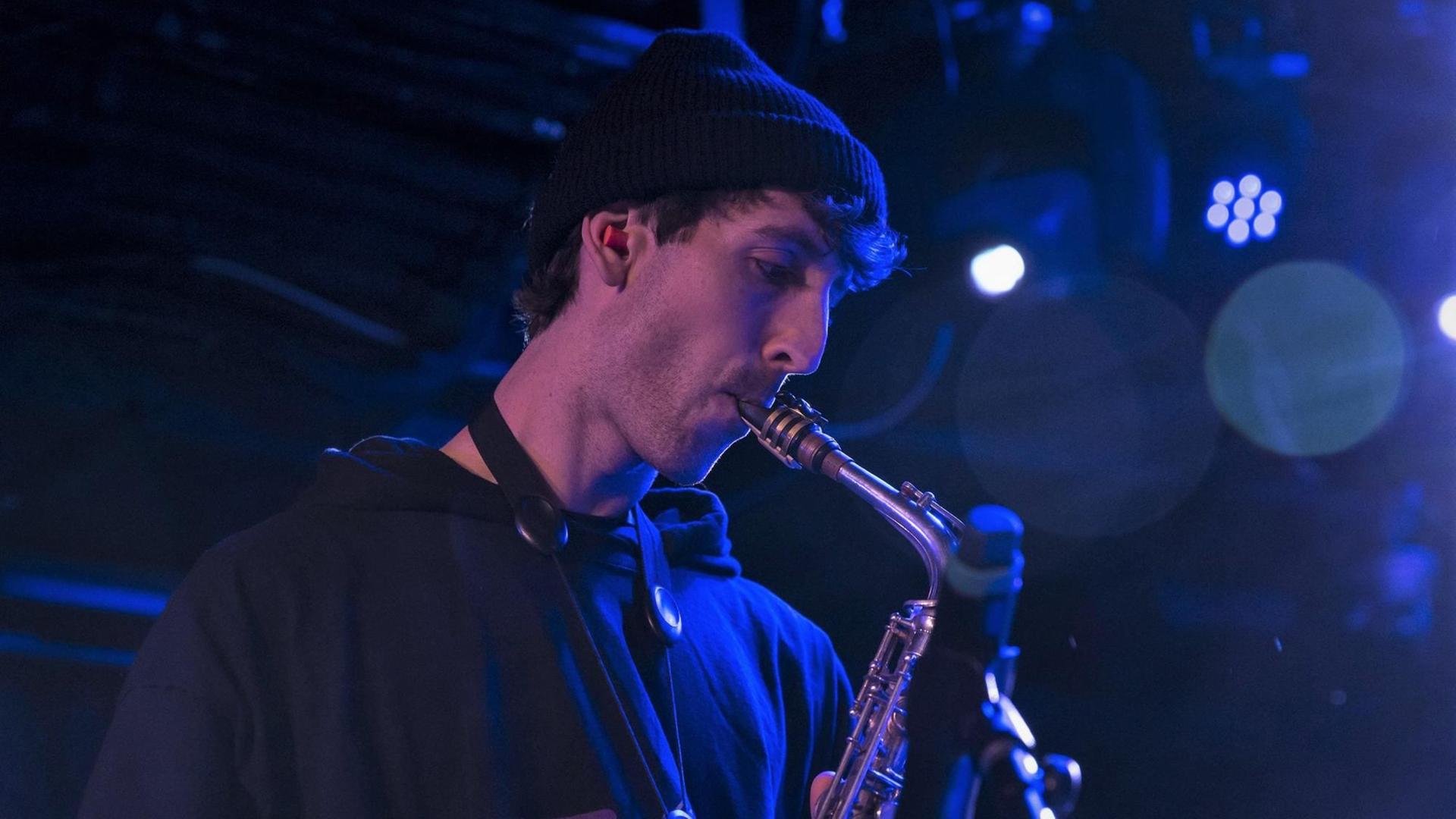 Der Jazz-Musiker Sam Gendel spielt Saxofon auf einer Bühne, teilweise in blaues Licht getaucht.