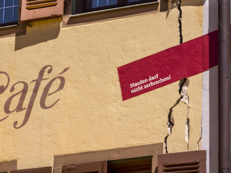 Detail einer Fassade mit Riss. Ein Pflaster über den Riss trägt die Aufschrift „Staufen darf nicht zerbrechen!“