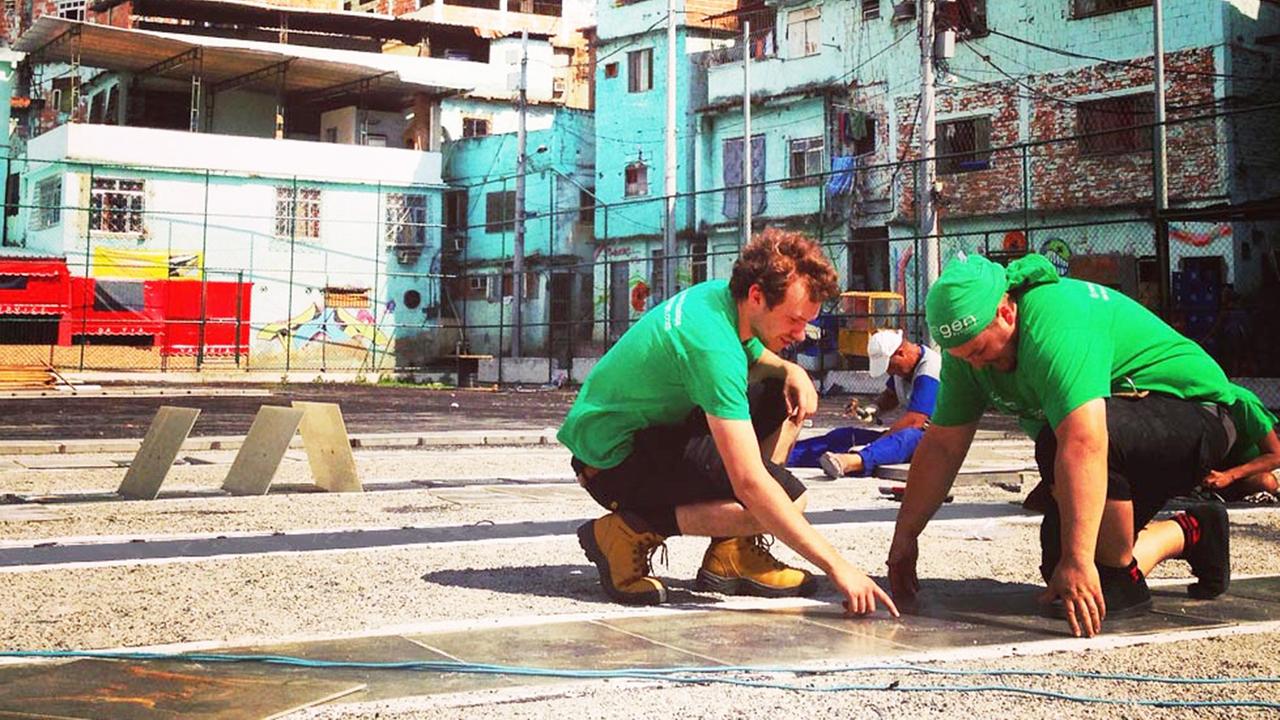 Zwei Männer in grünen T-Shirts verlegen Kinetik-Platten auf einem Fußballplatz in Rio de Janeiro verlegt Zwei Männer in grünen T-Shirts verlegen Kinetik-Platten auf einem Fußballplatz in Rio de Janeiro verlegt