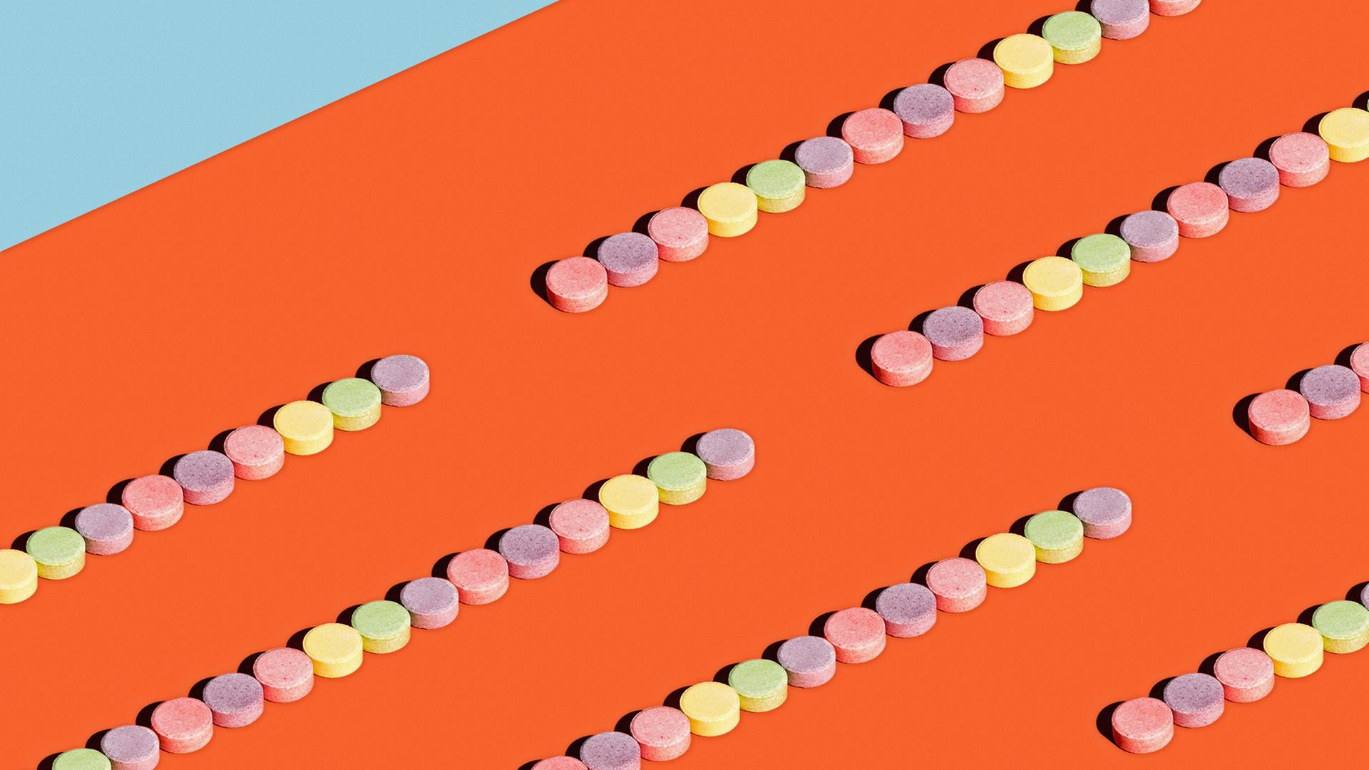Bunte Pastillen, die auf einer orangen Unterlage in Reihen geordnet sind Bunte Pastillen, die auf einer orangen Unterlage in Reihen geordnet sind