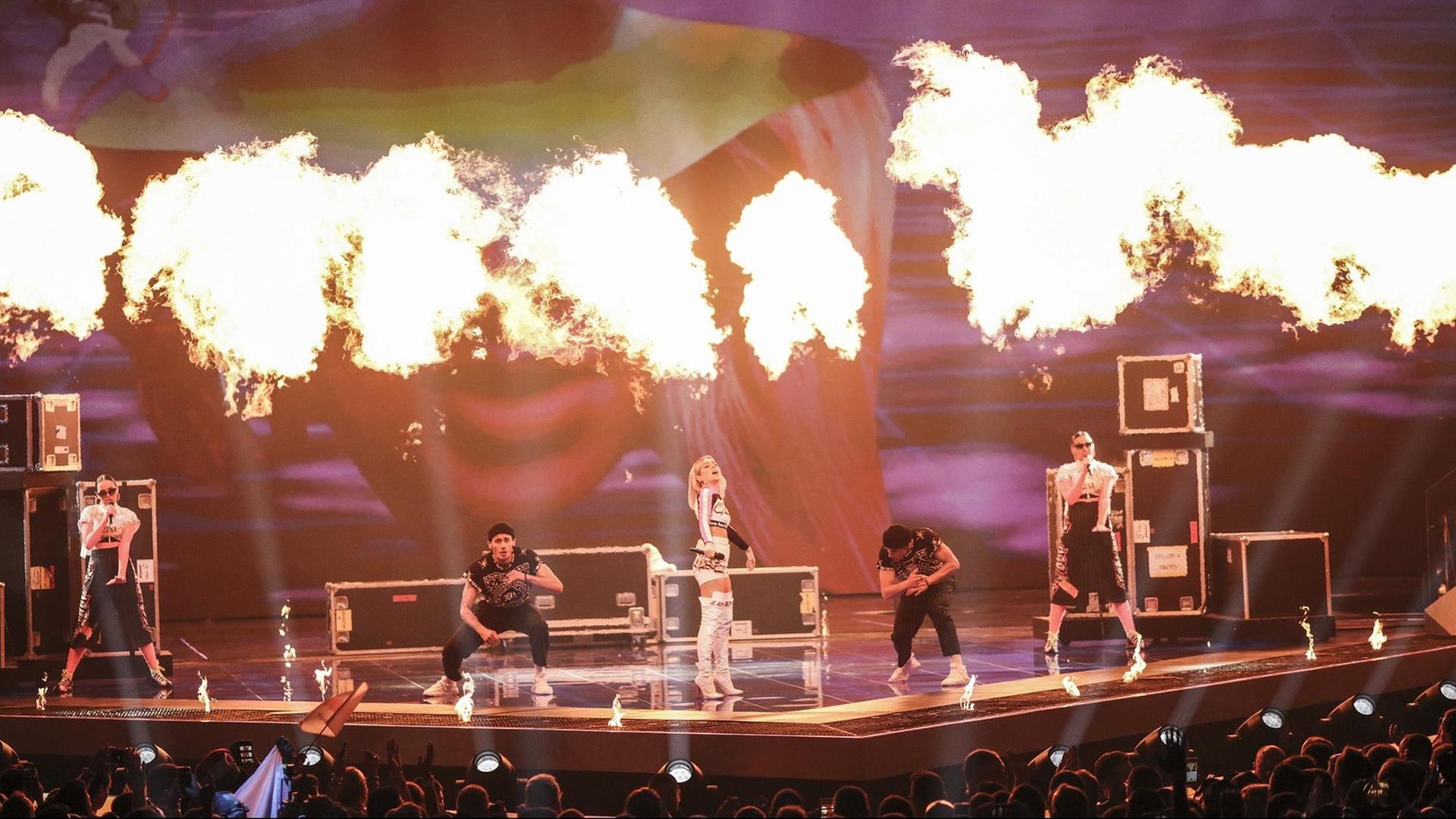 Auftritt der weißrussischen Sängerin ZENA im ersten Halbfinale des Eurovision Song Contest 2019, umrahmt von vier Tänzern, hinter ihnen lodern Flammenbälle. Auftritt der weißrussischen Sängerin ZENA im ersten Halbfinale des Eurovision Song Contest 2019, umrahmt von vier Tänzern, hinter ihnen lodern Flammenbälle.