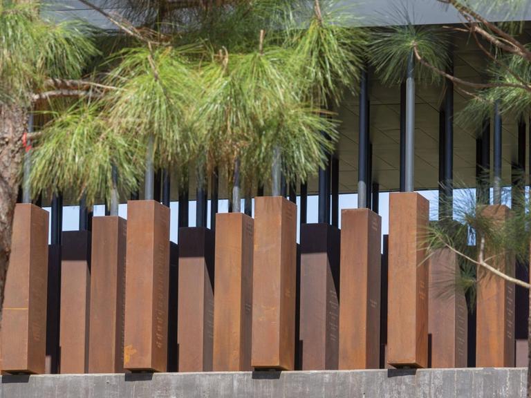 Blick auf das "National Memorial for Peace and Justice" in Montgomery, Alabama, mit Stahlkörpern und Bäumen davor