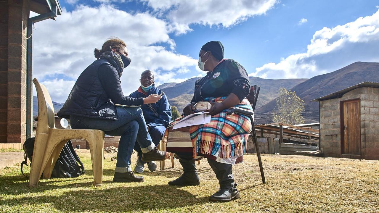 Sie sitzen im Dorf vor einer Hütte auf einfachen Stühlen. Im Hintergrund die Berglandschaft von Lesotho. Sie sitzen im Dorf vor einer Hütte auf einfachen Stühlen. Im Hintergrund die Berglandschaft von Lesotho.