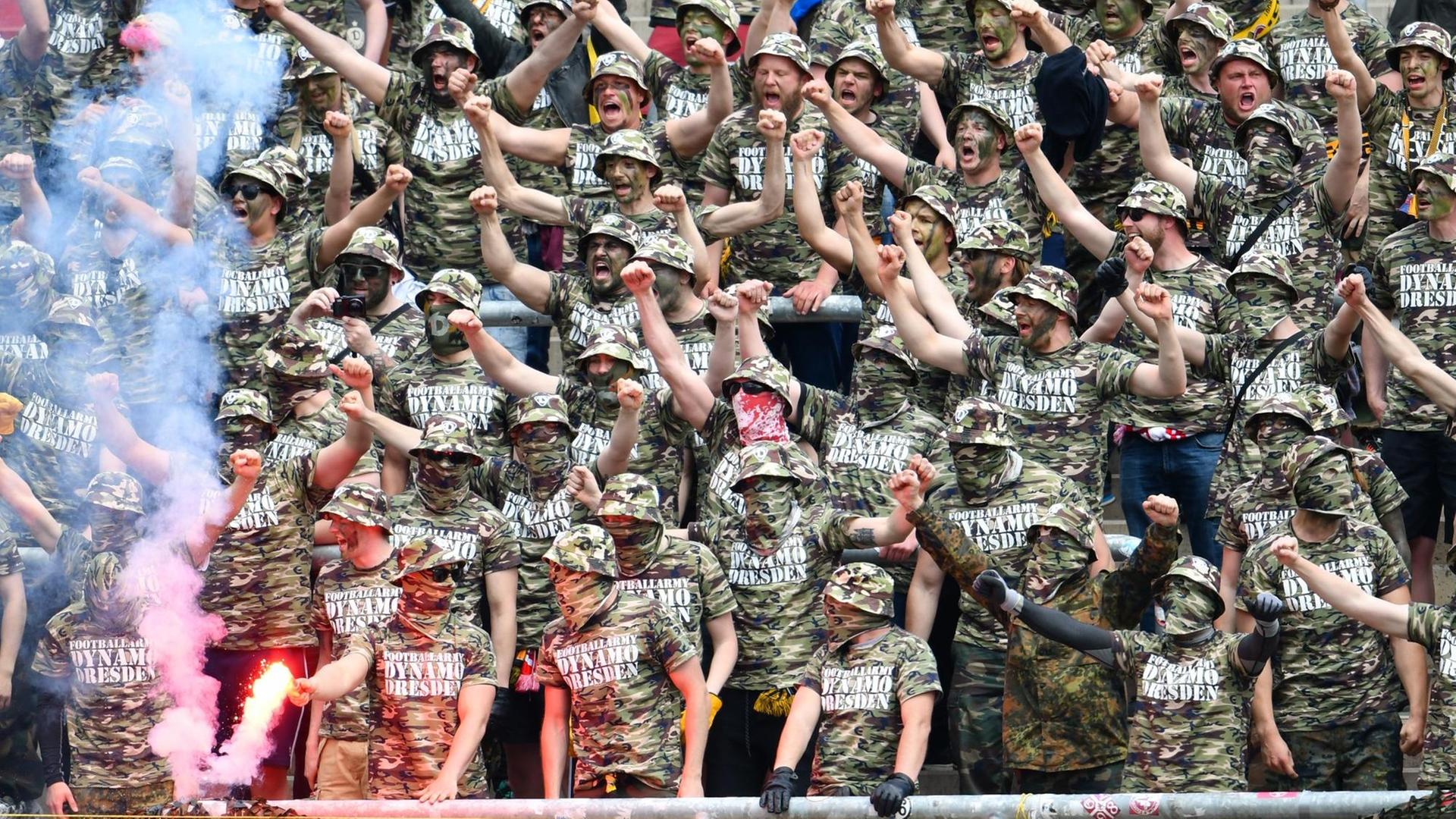Dresdener Fans in Tarnkleidung stehen während des Spiels auf der Tribüne und strecken die Fäuste in die Höhe. Dresdener Fans in Tarnkleidung stehen während des Spiels auf der Tribüne und strecken die Fäuste in die Höhe.