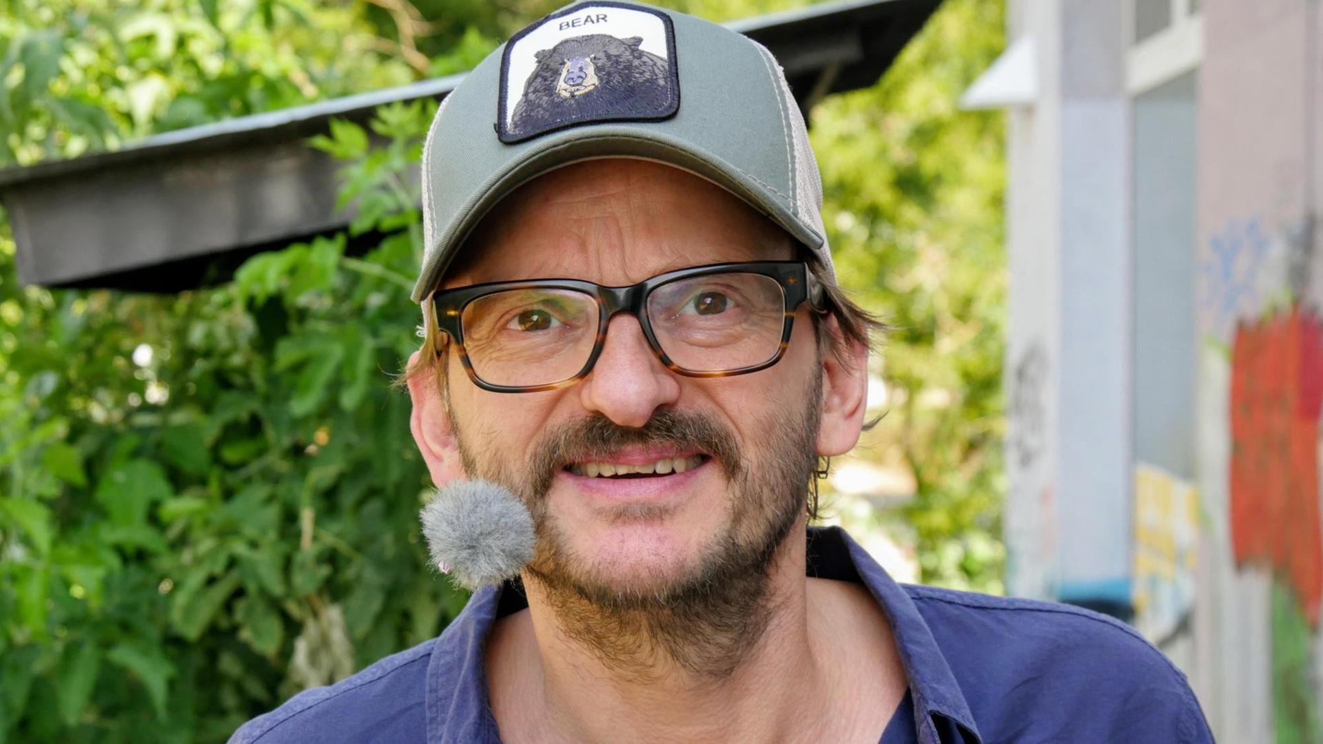 Der Schauspieler Milan Peschel schaut in die Kamera, er trägt eine Basecap, auf die ein Bär gedruckt ist. Der Schauspieler Milan Peschel schaut in die Kamera, er trägt eine Basecap, auf die ein Bär gedruckt ist.