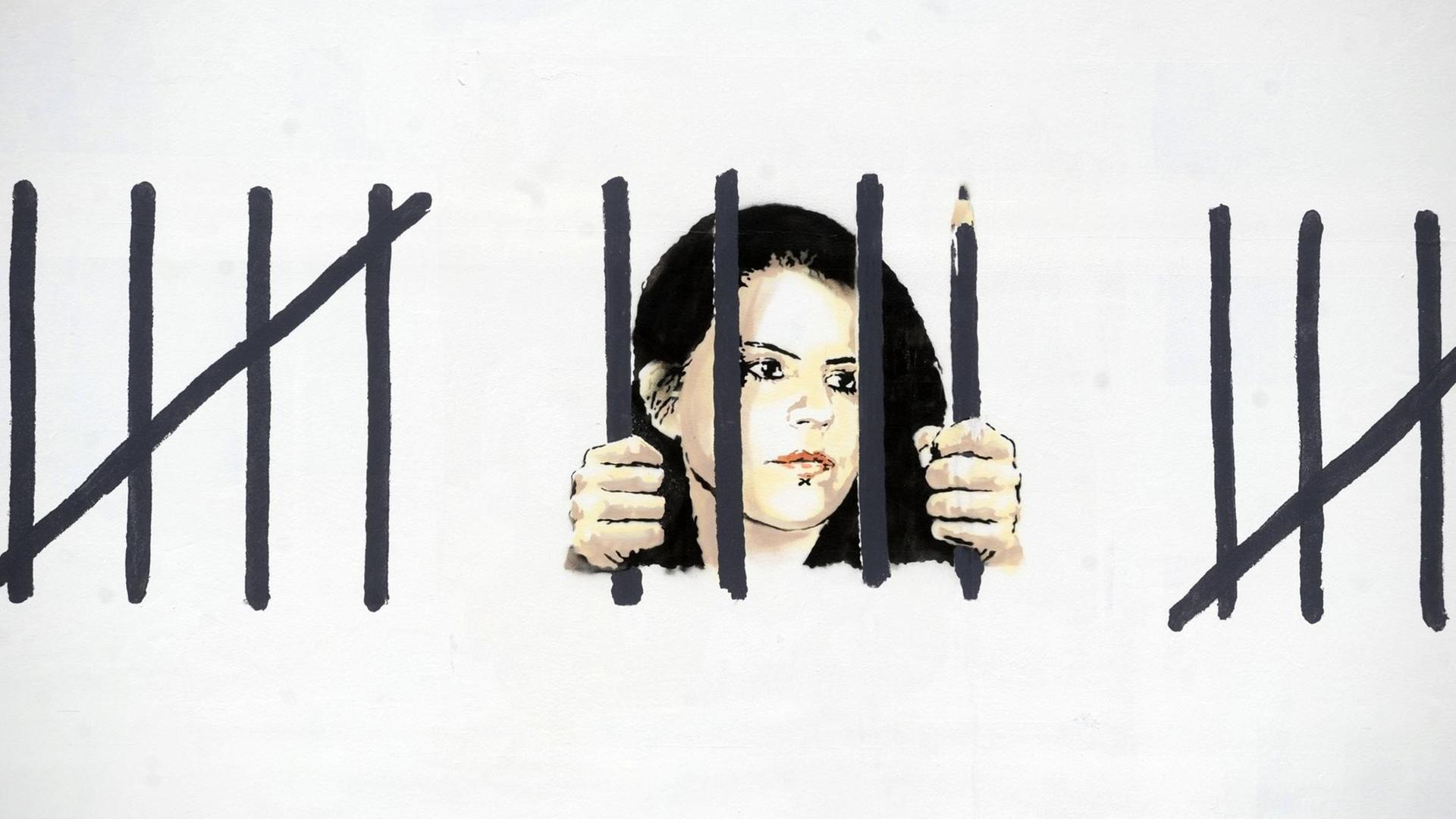 Foto eines Banksy Graffitis, das Zehra Doğan hinter Gittern zeigt. Foto eines Banksy Graffitis, das Zehra Doğan hinter Gittern zeigt.