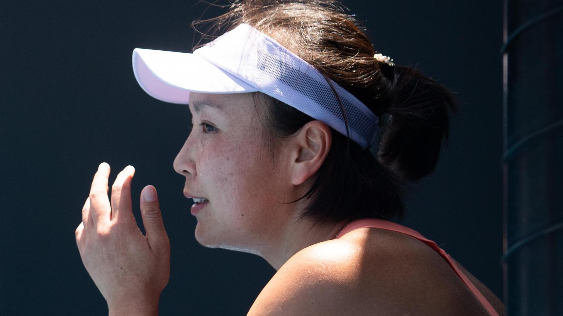 Peng Shuai trägt eine Schirm-Mütze und hält ihre Hand vor das Gesicht. Peng Shuai trägt eine Schirm-Mütze und hält ihre Hand vor das Gesicht.