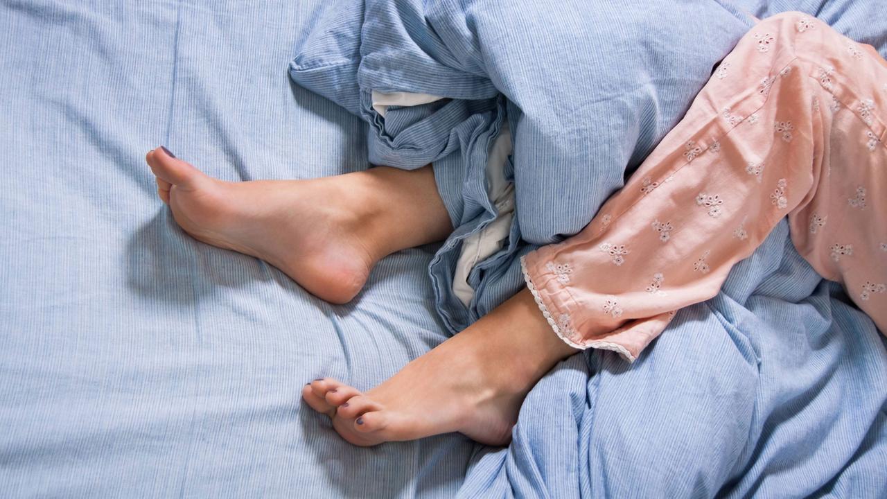 Weibliche Füße mit Schlafanzug im Bett am Morgen in blauer Bettwäsche