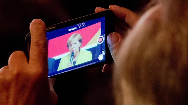 Bundeskanzlerin Angela Merkel (CDU) ist am 27.09.2017 während ihrer Rede in der Halle 39 in Hildesheim (Niedersachsen) auf dem Smartphone-Display eines Zuschauers zu sehen.