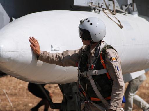 Ein russischer Pilot vor einem Einsatz in Syrien. Er trägt einen Helm und lehnt am Flugzeug.