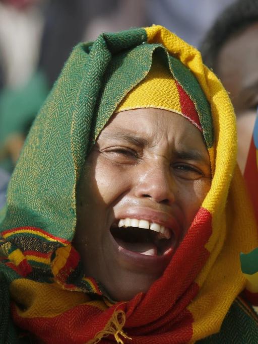 Eine junge Frau hat ein Tuch in den äthiopischen Nationalfarben um den Kopf geschlungen und reckt den Arm in die Höhe.