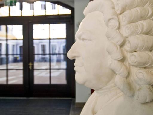 In einem historischen Hof mit grozügiger Eingangspassage steht die weiße Büste Johann Sebastian Bachs mit der typischen barocken Locken-Perrücke.