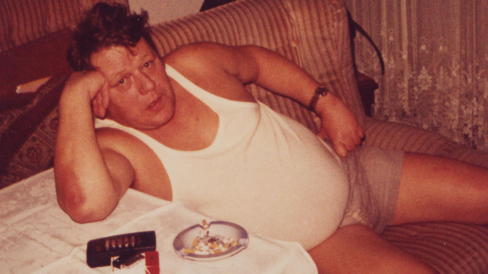 In einem Ausschnitt aus dem Film "Mein Papi" von 1981 von Jörg Buttgereit ist ein Mann im weißen Feinrippunterhemd und Shorts auf einem Wohnzimmersessel zu sehen. Der Film ist ebenfalls in der Undergroundfilm-Reihe im Lenbachhaus zu sehen. In einem Ausschnitt aus dem Film "Mein Papi" von 1981 von Jörg Buttgereit ist ein Mann im weißen Feinrippunterhemd und Shorts auf einem Wohnzimmersessel zu sehen. Der Film ist ebenfalls in der Undergroundfilm-Reihe im Lenbachhaus zu sehen.