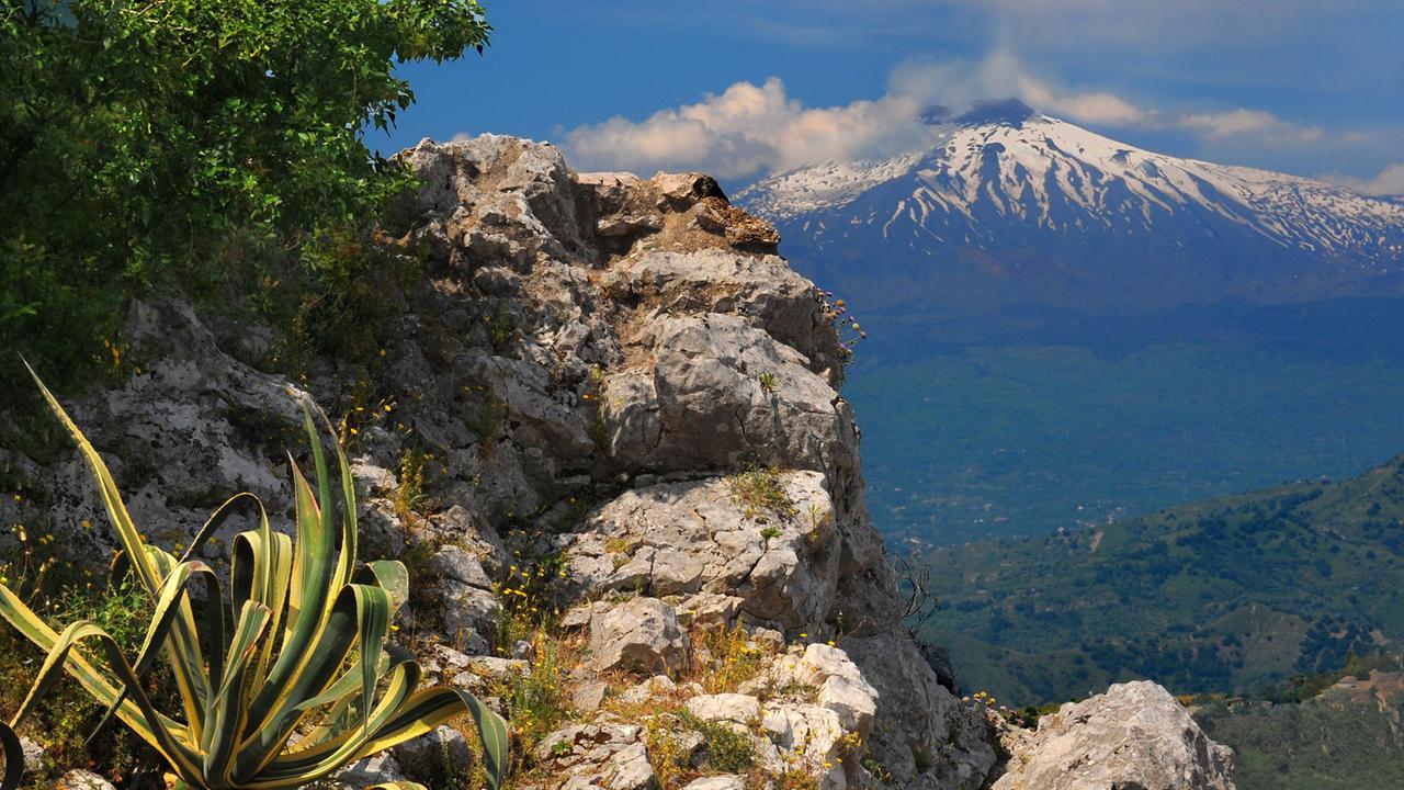 Der Ätna, mit 3340 Meter Höhe der größte Vulkan Europas, zeigt besonders von der Stadt Taormina seine ganze Schönheit. Zwischen den Ruinen des antiken Griechischen Theaters steht der schneebedeckte Berg im Kontrast zu der vielfältigen mediterranen Vegetation des wohl schönsten Ortes der Insel.