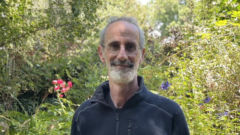 Ein älterer schlanker Mann mit weißem Haar, Bart und Brille steht in einer grünen Landschaft. Ein älterer schlanker Mann mit weißem Haar, Bart und Brille steht in einer grünen Landschaft.