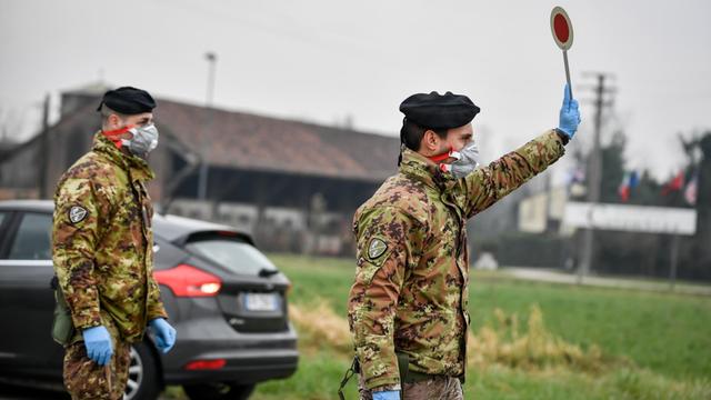 Ein Soldat mit Atemschutzmaske hält an einer Straßensperre vor der roten Zone von Turano Lodigiano eine Winkerkelle in die Höhe.