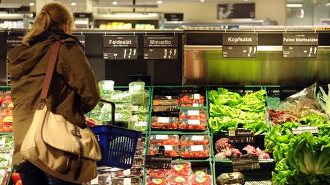 Ein Kundin steht in einem Supermarkt vor einer Auslage mit Salat.