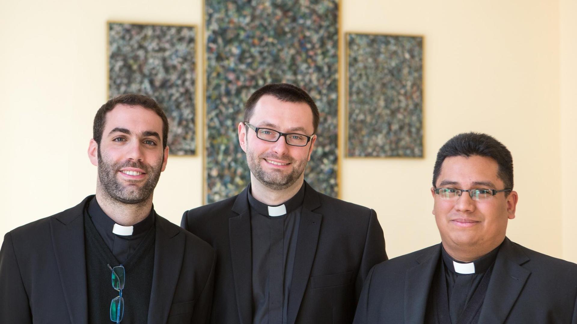 Die drei Priesteramtskandidaten Giovanni Donadel, Krzysztof Gaul und Ronald Prado Palma (v.l.) vor einem Kreuz in einem Kirchenraum