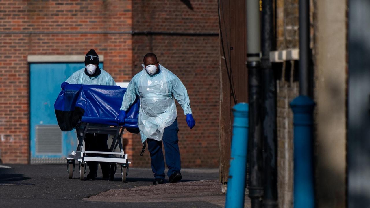 Zwei Krankenhausmitarbeiter des Lewisham-Krankenhauses in London schieben in Schutzkleidung einen Wagen, der für den Transport von Leichen verwendet wird, zur provisorischen Leichenhalle. Das Krankenhaus hat dafür einen Kühlcontainer auf seinem Parkplatz aufgestellt. Zwei Krankenhausmitarbeiter des Lewisham-Krankenhauses in London schieben in Schutzkleidung einen Wagen, der für den Transport von Leichen verwendet wird, zur provisorischen Leichenhalle. Das Krankenhaus hat dafür einen Kühlcontainer auf seinem Parkplatz aufgestellt.