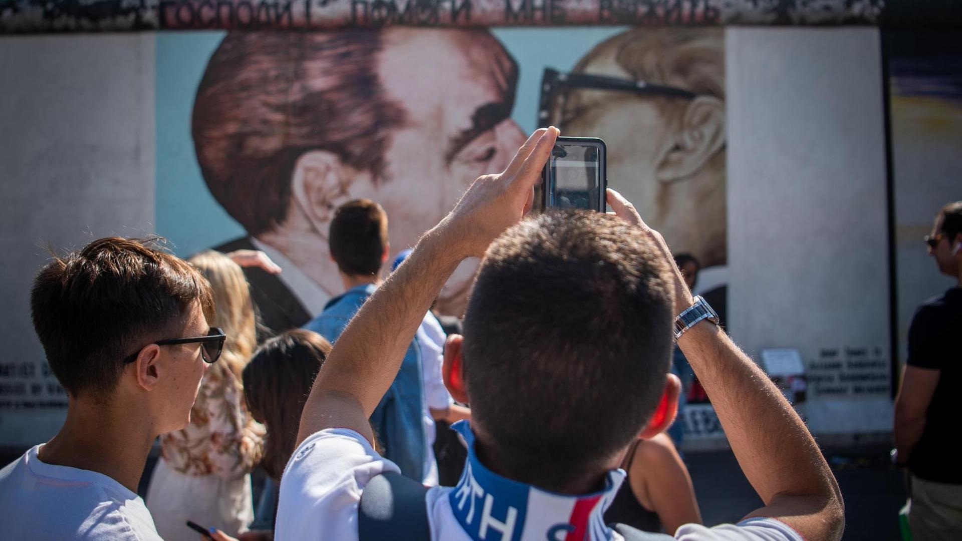 Touristen und Besucher stehen vor dem sogenannten "Bruderkussgemälde" an der East Side Gallery. Vor fast 30 Jahren hatten sich hier Künstler verewigt und das längste noch erhaltene Teilstück der Berliner Mauer mit ihren Kunstwerken umgedeutet. Touristen und Besucher stehen vor dem sogenannten "Bruderkussgemälde" an der East Side Gallery. Vor fast 30 Jahren hatten sich hier Künstler verewigt und das längste noch erhaltene Teilstück der Berliner Mauer mit ihren Kunstwerken umgedeutet.